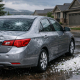 Stock photo of a hail-damaged car with dents and a cracked windshield in a Colorado neighborhood, captured after a storm with wet pavement and cloudy skies.
