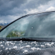 Close-up stock photo of a car windshield with a chip and hailstones on the hood, outdoors in a Colorado suburb with stormy spring sky.